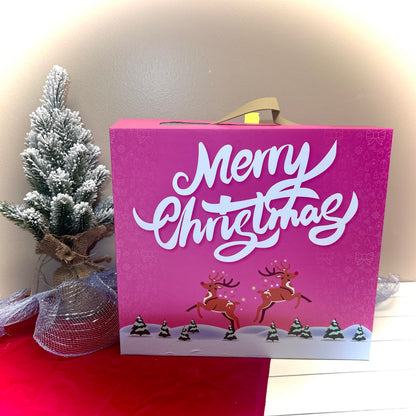 Pink Christmas advent calendar with reindeer and 'Merry Christmas' text, placed on a red surface with a small tree in the background.